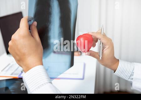 Medizinisches und medizinisches Versorgungskonzept. Der Arzt hält den Herzball und erklärt dem Patienten die Röntgenergebnisse, während er am Tisch im Büro sitzt. Stockfoto