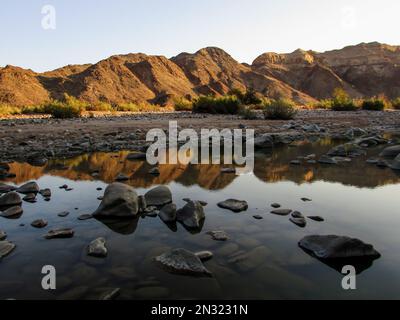 Die ruhige Landschaft mit Bergen, die sich in den Fish River spiegeln, vom Fuße des Canyons in Namibia aus gesehen Stockfoto