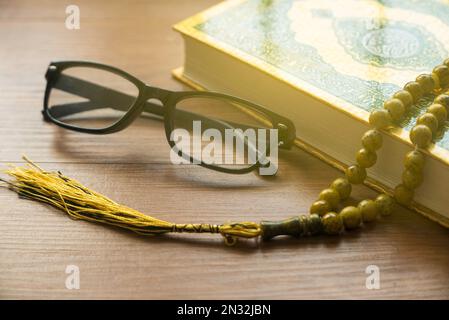 Selektiver Fokus von Rosenkranzperlen, Gläsern und Koran auf Holzhintergrund. Stockfoto