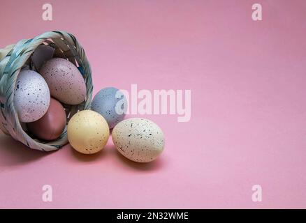 Ostereier in einem Korb an der Seite isoliert auf pinkfarbenem Hintergrund. Stockfoto