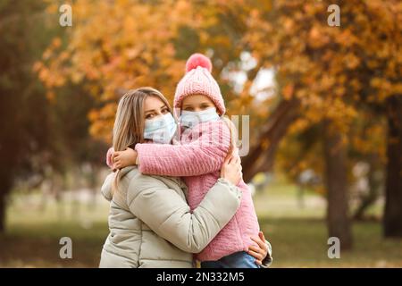 Mutter und Tochter in medizinischen Masken im Freien am Herbsttag. Schutzmassnahmen während der Coronavirus-Quarantäne Stockfoto