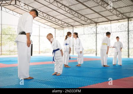 Kinder und Trainer im Kimono führen Ritualbogen vor dem Karate-Training auf Tatami im Freien Stockfoto