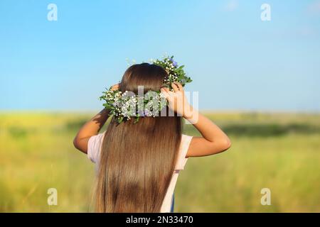 Süßes kleines Mädchen mit Blumenkranz draußen, Rückansicht. Das Kind verbringt Zeit in der Natur Stockfoto