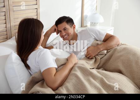 Glückliches Paar mit warmem beigefarbenem Karomuster, das im Bett lag Stockfoto