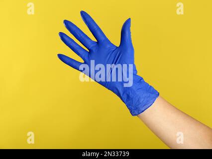 Frau in blauen Latexhandschuhen auf gelbem Hintergrund, Nahaufnahme der Hand Stockfoto
