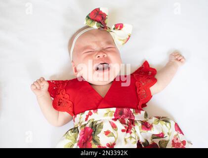 Weinendes weißes neugeborenes Mädchen in einem roten Kleid. Weinendes Kind. Stockfoto
