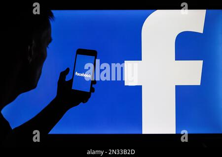 Vilnius, Litauen - 2022. Februar 6: Facebook- und Meta-Firmenlogo auf Smartphone- und PC-Bildschirmen. Männersilhouette mit facebook-App in der Hand Stockfoto