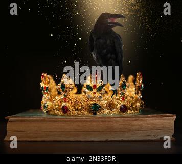 Fantasiewelt. Schwarze Krähe, beleuchtet von magischem Licht, das auf der goldenen Krone sitzt Stockfoto