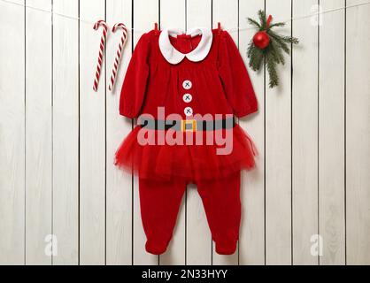 Süße Weihnachtskleidung für Babys, Tannenäste und Zuckerstangen, die an weißen Holzwänden hängen Stockfoto