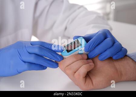 Arzt überprüft Sauerstoffgehalt des Patienten mit dem Pulsoxymeter am hellgrauen Tisch, Nahaufnahme Stockfoto