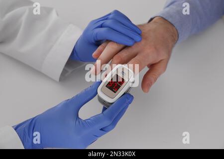 Arzt überprüft Sauerstoffgehalt des Patienten mit dem Pulsoxymeter am hellgrauen Tisch, Nahaufnahme Stockfoto