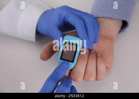 Arzt überprüft Sauerstoffgehalt des Patienten mit dem Pulsoxymeter am hellgrauen Tisch, Nahaufnahme Stockfoto