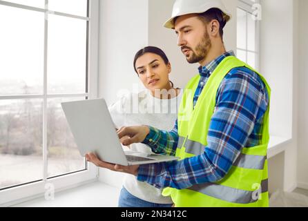 Baumeister oder Architekt zusammen mit einer jungen Frau, die über den Hausbau diskutiert und ein Notebook verwendet Stockfoto