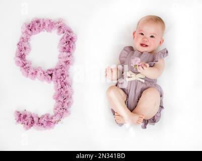 Kleines neugeborenes Mädchen in einem lila Strampelanzug. 9 Monate altes Baby. Neun Monate Baby-Meilenstein. Stockfoto