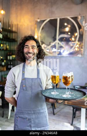 Vertikale Aufnahme eines jungen Kellners, der ein Serviertablett mit Bier hält Stockfoto