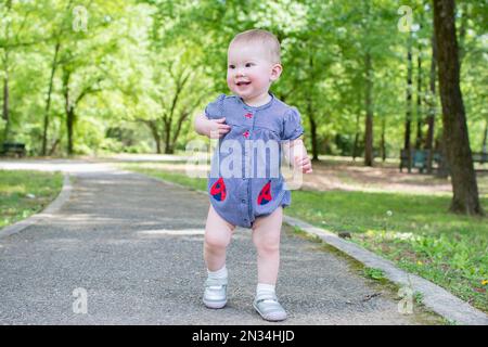 Süßes, weißes Baby, das die ersten Schritte im Park macht. Gehen eines Kleinkindes Stockfoto