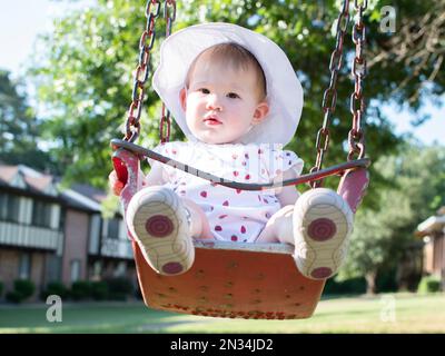 Ein weißes Mädchen, das an einem sonnigen Sommertag in einer Schaukel sitzt Stockfoto