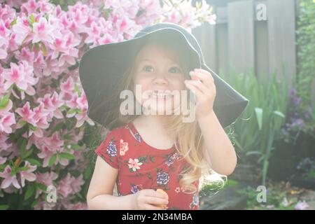 Lächelndes, süßes, weißhäutiges, blondes Kleinkind mit Hut, das den Sommer und den sonnigen Tag draußen genießt Stockfoto