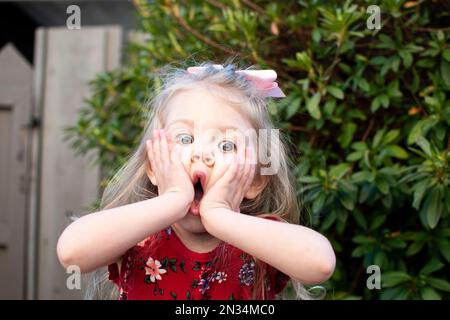 Ein überraschtes kleines Mädchen, das ihre Wangen mit den Händen hält. Stockfoto