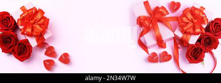 Grußkarte zum Valentinstag, Muttertag und Geburtstag. Rote Rosen, Geschenkschachteln mit einer Schleife aus rotem Satinband auf pinkfarbenem Hintergrund. Banner Stockfoto