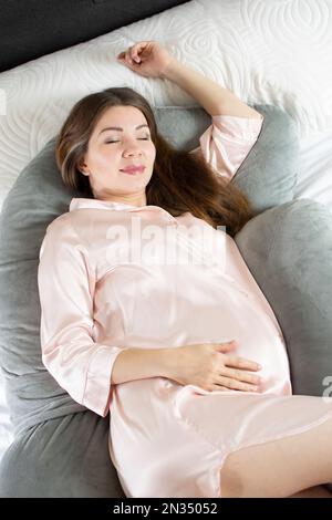 Weiße Schwangere, die in einem Schwangerschaftskissen schläft. Schlafkomfort in der Schwangerschaft. Umstandskissen Stockfoto