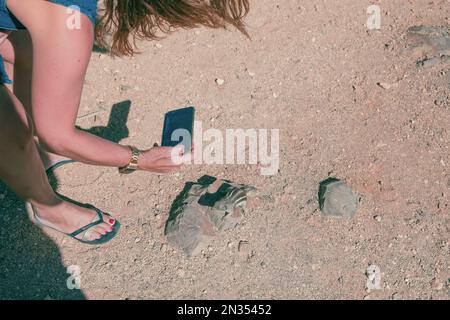 Detail einer jungen Frau, die ein Eichhörnchen mit der Hand füttert, während sie ein Foto mit ihrem Mobiltelefon in Fuerteventura macht. Natürliche Ressourcen der Kanarischen Inseln.