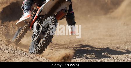 Der Rennfahrer auf dem Motorrad nimmt am Motocross-Rennen Teil, an aktivem Extremsport, an fliegenden Trümmern von einem Motocross auf einer Schotterbahn Stockfoto