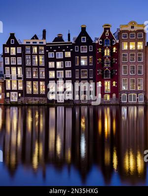 Amsterdam, Niederlande - 18. Januar 2023: Stadtbild traditioneller holländischer Häuser zur blauen Stunde am Damrak-Kanal in Amsterdam mit Reflexion Stockfoto