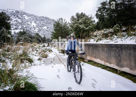 Radfahrer im Schnee neben dem Wasserkanal, dem Gorg Blau Reservoir, Escorca, Mallorca, Balearen, Spanien Stockfoto