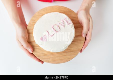 Das Mädchen hält einen Bento-Kuchen mit der Inschrift "Liebe und Herzen". Ein kleiner koreanischer Kuchen für eine Person. Ein süßes Dessertgeschenk für einen geliebten Menschen für jeden Stockfoto