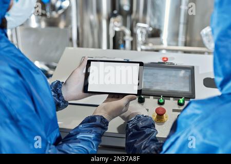Nahaufnahme eines Arbeiters, der ein digitales Tablet hält, mit einem Modell mit weißem Bildschirm in einem Industriebetrieb Stockfoto