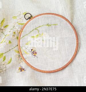 Hoops mit Holzstickerei, Draufsicht, Nadel mit Faden und Stoff mit Blumenmuster, Stickerei von Hand. Hobby und Handarbeit Stockfoto