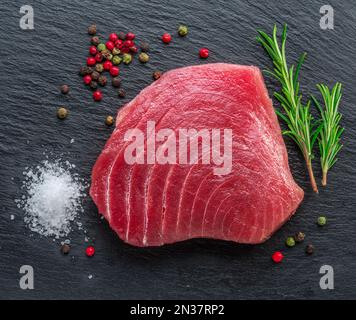 Rohes Thunfischsteak auf einem Servierteller aus schwarzem Naturstein. Draufsicht. Stockfoto