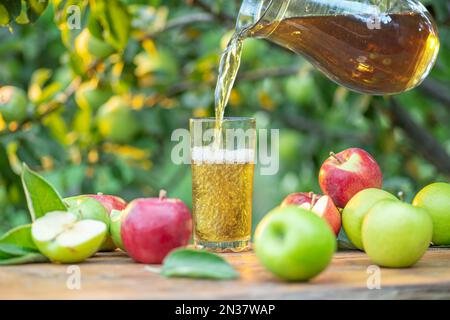 Apfelsaft in das Glas gießen. Frische Bio-Äpfel und ein Glas Apfelsaft auf einem Holztisch im Sommergarten. Stockfoto