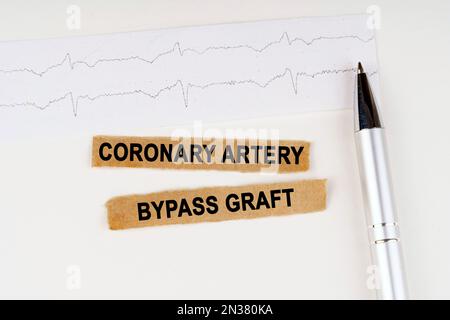 Medizinisches Konzept. Auf dem EKG liegt ein Stift und zerrissenes Papier mit dem Text - Koronararterien-Bypass-Transplantat Stockfoto