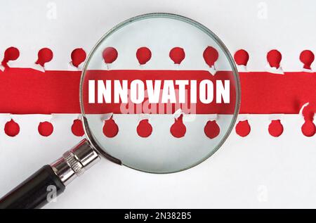 Zwischen zwei Blättern eines Notizbuchs auf einem roten Streifen mit der Aufschrift „Innovation“ befindet sich eine Lupe. Stockfoto