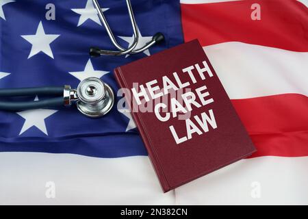 Regelkonzept. Auf der US-Flagge liegt ein Stethoskop und ein Buch mit der Inschrift - GESUNDHEITSGESETZ Stockfoto