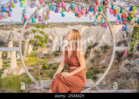 Junge Frau, die das Tal mit Felsformationen und Feenhöhlen in der Nähe von Goreme in Kappadokien, Türkei, erkundet. Wunschbaum. Kleine mehrfarbige Kannen mit Stockfoto