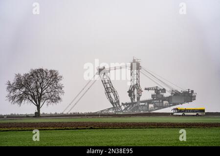 Bagger im Braunkohlebergwerk Garzweiler II im ehemaligen zerstörten Dorf Lützerath, an der Landstraße L12, im Nebel, Bus der Linie Stockfoto