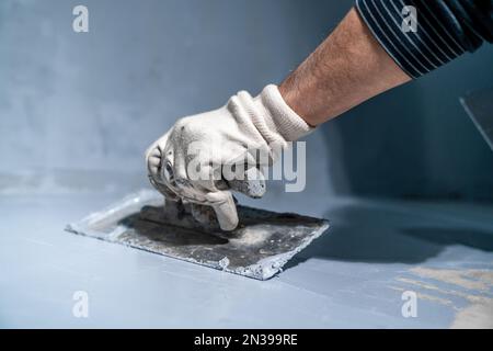 Verteilen der Dämmung auf dem Beton auf dem Boden mit einer Kelle Stockfoto