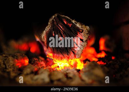 Holz auf Feuer und lebende Kohlen in einem holzbefeuerten Kamin auf schwarzem dunklem Hintergrund Stockfoto