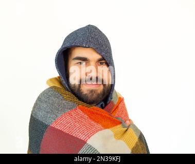 Junger bärtiger Mann in Winterkleidung mit blauer Decke. Kalter Ausdruck. Ich schaue in die Kamera. Isolierter weißer Hintergrund. Stockfoto