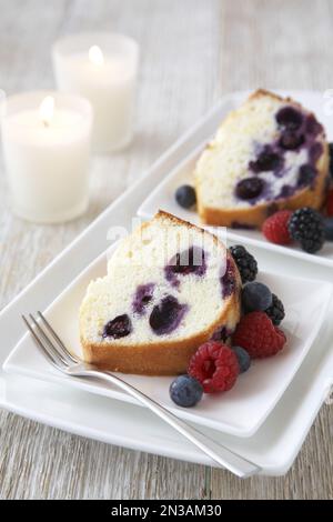 Vanille-gebündelter Kuchen mit gemischten Beeren auf weißem Teller mit einer Gabel Stockfoto