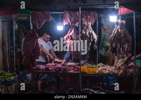 Ein Metzger schneidet rohes Fleisch mit einem Fleischbeil auf dem wichtigsten Gemüse- und Fleischgroßmarkt Phsar Dumkor nachts in Phnom Penh, Kambodscha. © Kraig Stockfoto