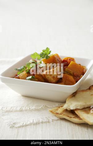 Hähnchen-Curry in quadratischer Schüssel, serviert mit Pita-Brot Stockfoto