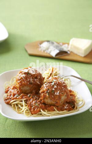 Spaghetti und Fleischbällchen mit Parmasekäse in einer roten Tomatensoße auf einem weißen Teller mit grüner Tischdecke aus Leinen Stockfoto