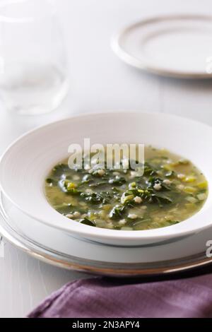 Schüssel mit grüner Blattsuppe mit sternförmiger Pasta auf weißem Hintergrund und einer violetten Serviette Stockfoto