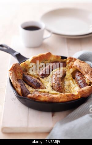 Gebackene Wurst und Pfannkuchen zum Frühstück in gusseiserner Pfanne mit einer Tasse Kaffee Stockfoto