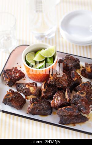 Rinderrippchen mit Gewürzreiben, serviert mit Limettenspalten auf einer Platte Stockfoto