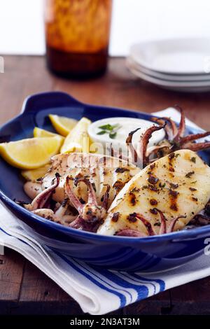 Gegrillte Calamari mit Zitronenkeilen in einer blauen Schüssel Stockfoto